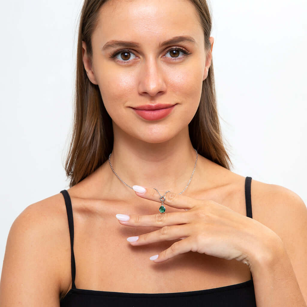 Woman wearing a necklace with an emerald birthstone pendant.