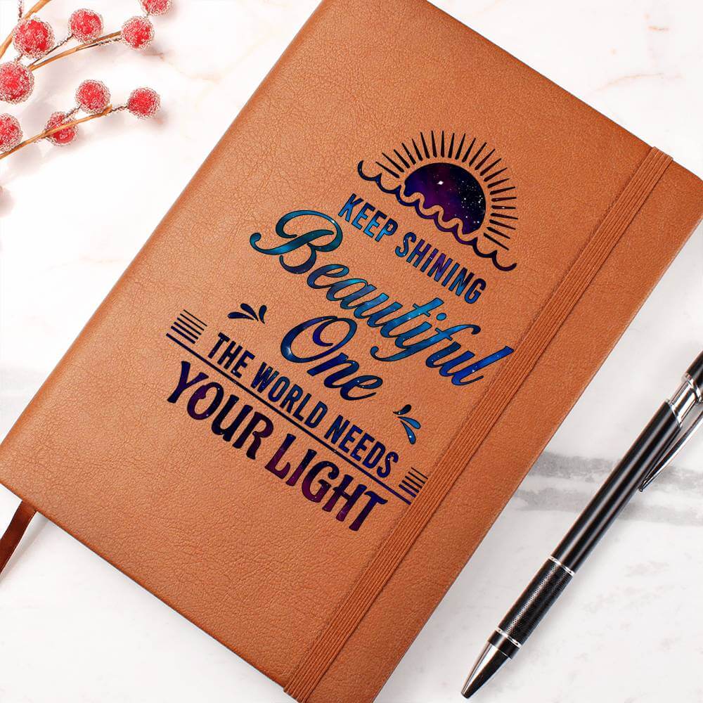 Keep Shining Beautiful One - Graphic Leather JournalVenture beyond with the Graphic Leather Journal. Ideal for goal setting and organization, it features a bookmark and elastic closure.Moving Phrases