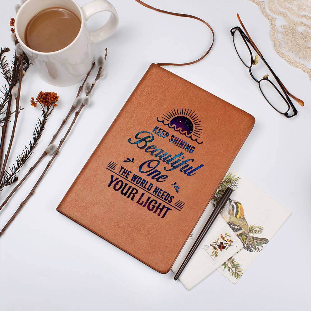 Keep Shining Beautiful One - Graphic Leather JournalVenture beyond with the Graphic Leather Journal. Ideal for goal setting and organization, it features a bookmark and elastic closure.Moving Phrases