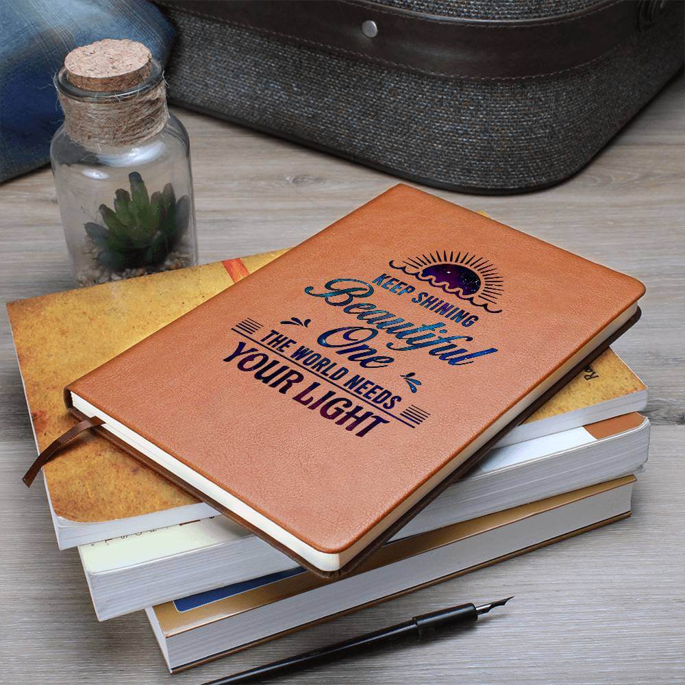 Keep Shining Beautiful One - Graphic Leather JournalVenture beyond with the Graphic Leather Journal. Ideal for goal setting and organization, it features a bookmark and elastic closure.Moving Phrases