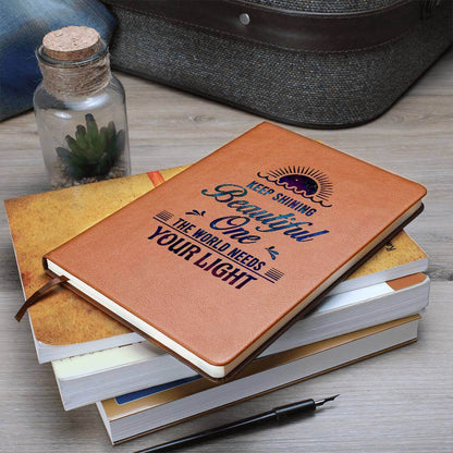 Keep Shining Beautiful One - Graphic Leather JournalVenture beyond with the Graphic Leather Journal. Ideal for goal setting and organization, it features a bookmark and elastic closure.Moving Phrases