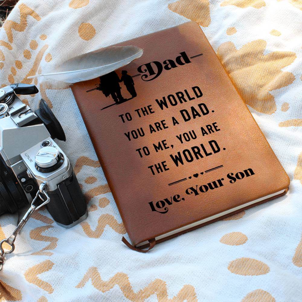 Dad, to the World you are - Graphic Leather JournalVenture beyond with the Graphic Leather Journal. Ideal for goal setting and organization, it features a bookmark and elastic closure.Moving Phrases